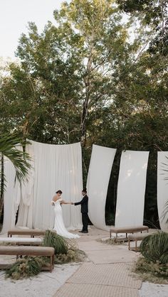 a bride and groom holding hands in front of white drapes at their outdoor wedding ceremony