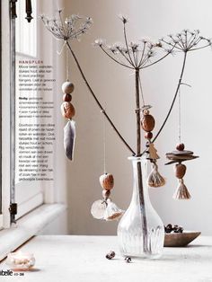 a glass vase filled with dried flowers on top of a white table next to a window