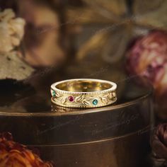 a gold wedding band with green and red stones sits on top of a wooden box