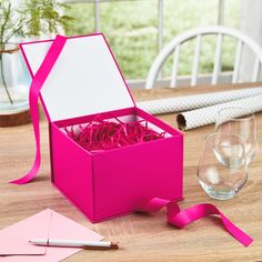 a pink box filled with paper and scissors on top of a wooden table next to wine glasses