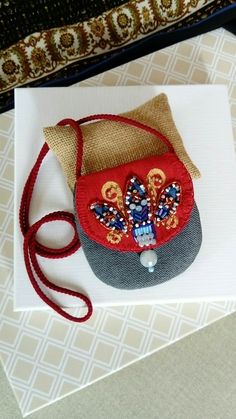 a small red purse sitting on top of a white table next to a brown bag