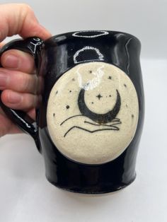 a hand holding a black and white coffee mug with a crescent moon on the side