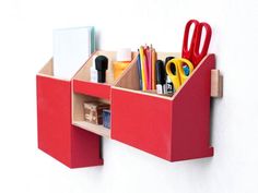 a red desk organizer with scissors, pencils and other office supplies in it on a white wall