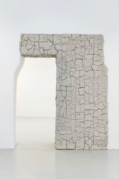 an abstract sculpture made out of concrete with a white wall behind it and a window in the middle