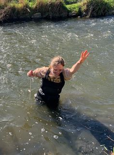 a woman is wading in the water with her arms out and she has one hand up