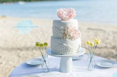 a wedding cake sitting on top of a white table next to the ocean and beach