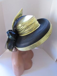 "Here is the chance to make a Statement--big time.  This church or derby hat grabs attention from the get go. The body of the hat is in black millinery weave. The 1 /2\" downturned brim is edged in gold lame' fabric. The lame' is also found in the wide pleated band circling the crown. Hold on --there is more. A stiff black net studded with gold sequins forms an anchor for a large bow at the back.  The 6 x 14\" bow in gold lame' is angled.  It anchors an 8\" black feather and a beaded petal in br Adjustable Vintage Hats For Races, Vintage Top Hat With Short Brim For Races, Retro Short Brim Hats For Church, Black Hats For Church And Kentucky Derby, Black Hat For Kentucky Derby Church Event, Retro Wide Brim Top Hat For Kentucky Derby, Black Hat For Church And Kentucky Derby, Vintage Top Hat For Kentucky Derby Races, Vintage Short Brim Top Hat For Races