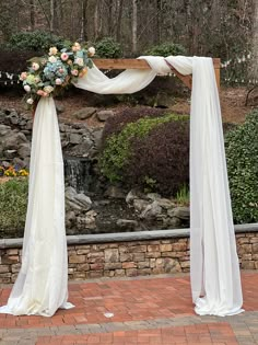 a wedding arch decorated with flowers and white draping on brick walkway next to water