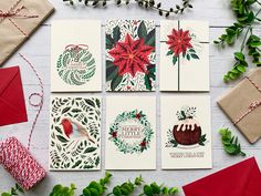 four christmas cards with envelopes on top of them, surrounded by greenery and decorations