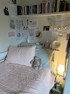 a bed with a pink comforter and stuffed animal sitting on top of it next to a book shelf filled with books