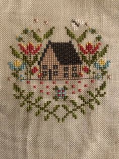 the house is surrounded by flowers and leaves on this cross stitched pillow cover,