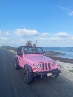 two people riding in the back of a pink jeep down a road next to the ocean