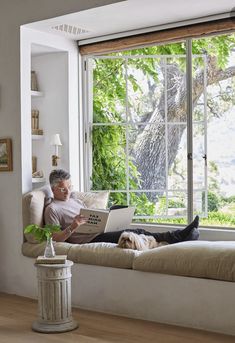 an older man sitting on a couch with his laptop in front of a large window