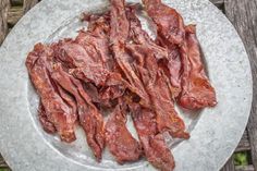 some meat is sitting on a plate on a wooden table with grass in the background