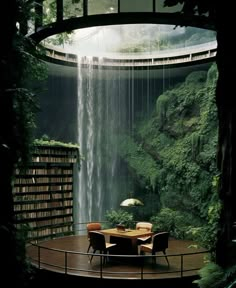 a table and chairs in front of a waterfall with bookshelves on the floor