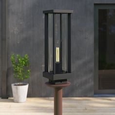 an outdoor post light with a plant in the middle on a wooden deck next to a building