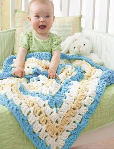 a baby sitting in a crocheted bed with a green and white blanket on it