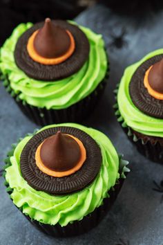 three cupcakes with green frosting and chocolate decorations on top, sitting on a table