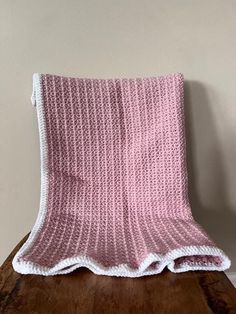 a pink and white knitted blanket sitting on top of a wooden table