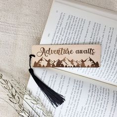 a bookmark with the words adventure awaits on it next to an open book