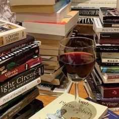 a glass of red wine sitting on top of a table next to a pile of books