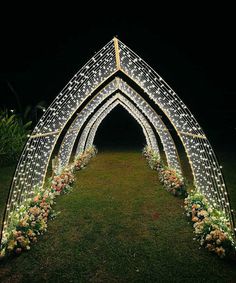 a lighted arch in the grass with flowers and greenery on either side at night