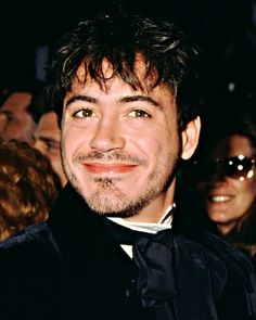 a man in a black suit and bow tie smiling at the camera with people behind him