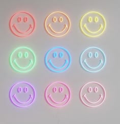 four different colored smiley faces on a white surface with neon lights in the shape of circles