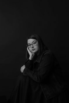 a black and white photo of a woman with glasses looking at the camera while leaning on her hand