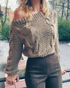 a woman is posing for the camera wearing a brown sweater and black pants with her hands in her pockets