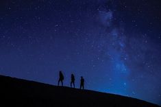 three people standing on top of a hill under a night sky with stars in the background