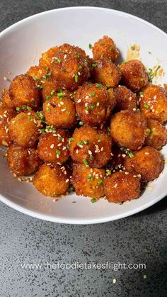 a white bowl filled with meatballs covered in sesame seeds and garnished with green onions