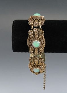 Presented is a stunning antique Chinese vermeil (gilt silver) and jade bracelet, dating to the late 1800s or early 1900s. The bracelet consists of five very ornate filigree links, each bezel set with a round cabochon of beautiful light green jade. The jade is a very appealing color, with natural mottling and variations but overall very well matched. The filigree is exceptionally intricate and finely done by hand, some of the highest quality you'll find. The bracelet closes with a tab insert styl Antique Cabochon Jewelry For Ceremonial Occasions, Elegant Cabochon Jewelry For Ceremonial Occasions, Bronze Bracelet For Formal Occasion, Antique Jewelry Bracelet With Intricate Design, Ornate Bronze Jewelry For Ceremonial Occasions, Collectible Intricate Design Jewelry Bracelet, Elegant Green Bracelets For Ceremonial Occasions, Victorian Jewelry With Intricate Design For Collectors, Jade Bracelet For Wedding