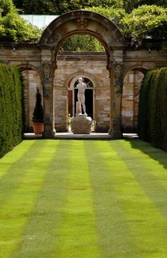 an outdoor garden with a statue in the center and hedges on both sides, surrounded by stone archways