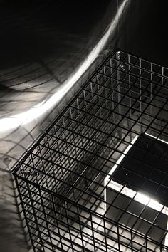 a black and white photo of a square object in a caged area with light coming through it