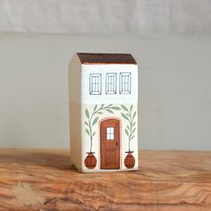 a small ceramic house sitting on top of a wooden table next to a white wall