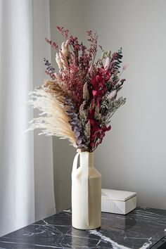 a vase filled with dried flowers on top of a marble table next to a book