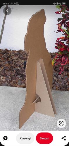 an animal made out of cardboard sitting on top of a cement ground next to flowers