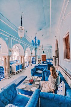 a woman sitting on a blue couch in a room with chandeliers hanging from the ceiling