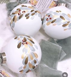 three white ornaments with gold leaf designs on them sitting on a marble counter top next to some green leaves