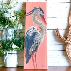 a painting of a blue heron on a pink background next to some flowers and a wicker basket