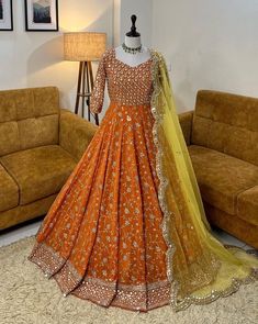 an orange and yellow lehenga is on display in front of a brown couch