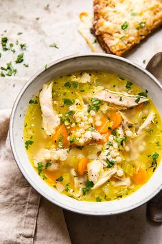 a white bowl filled with chicken and barley soup next to a slice of bread on a napkin