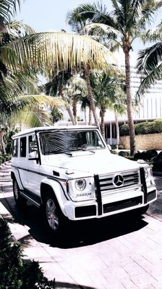 a white mercedes g - class parked in front of palm trees