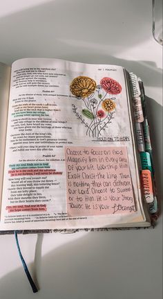 an open bible with writing on it and flowers in the pages next to some markers