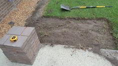 a brick box sitting in the middle of a yard next to a shovel and rake