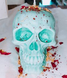 a white skull with blue eyes and red petals on the table next to a candle