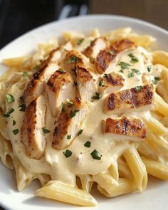 a white plate topped with pasta covered in sauce and chicken breast pieces on top of it