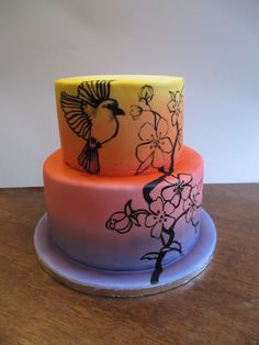 a three tiered cake decorated with flowers and birds on the top, sitting on a wooden table