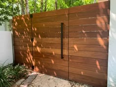 a wooden gate in front of a white wall and some plants on the side walk